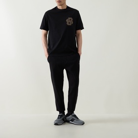 Model wearing Boss Black Casual black cotton-blend sweat bottoms, styled with matching black tee and grey trainers.