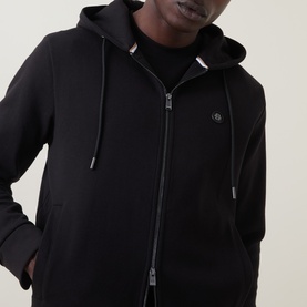 Model wearing Boss Black Casual black zip-through hoodie with drawstring hood, small logo badge, and front zip pockets.
