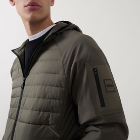 Model wearing Boss Green Label Urbanex Hybrid Quilted Jacket in Open Green, showing hooded collar, quilted bodice and sleeve logo badge detail.