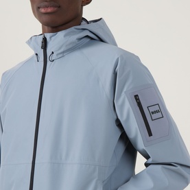 Model wearing Boss Green Label Visit JT Logo Jacket in dark grey, showing hood, front zip, and sleeve pocket with logo badge detail.