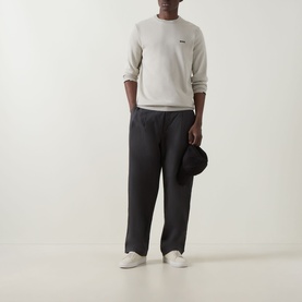 Model wearing Boss Green Label Ever-X Logo Sweater in Light Beige with dark navy trousers, white trainers, and holding a bucket hat.
