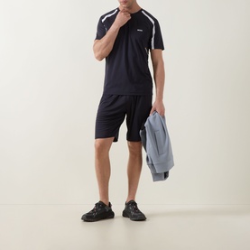 Model wearing Boss Green Label dark blue crew neck T-shirt with white shoulder panels, styled with matching shorts, carrying a grey jacket.