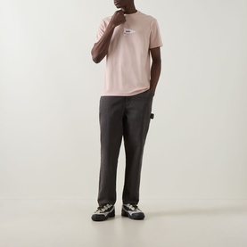 Model wearing Boss Green Label Light Pastel Orange crew neck T-shirt with dark grey carpenter trousers and chunky trainers.