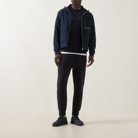 Model wearing Boss Green Label Salbo Logo Sweatshirt in dark blue, styled with navy zip-up jacket, black joggers and dark trainers.
