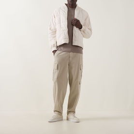 Model wearing Boss Green Label Light/Pastel Green cotton crew neck T-shirt, styled with cream quilted jacket, beige cargo trousers and white trainers.