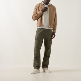 Model wearing Boss Green Label Logo Half-Zip Sweatshirt in Light Beige with olive cargo trousers, tan bomber jacket and white trainers.