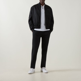 Model wearing Boss Green Label Ever-X Logo Zip Polo Shirt in white, styled with black bomber jacket and black tapered trousers, white trainers.