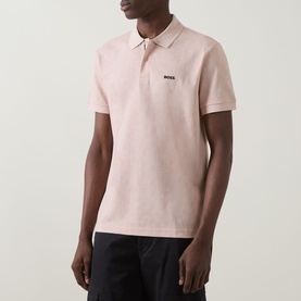 Model wearing Boss Green Label Swing Printed Logo Polo Shirt in light pastel orange, short sleeves, logo chest detail, styled with dark trousers.