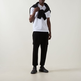 Model wearing Boss Green Label Swing Printed Logo Polo Shirt in white, styled with black cargo trousers, chunky black trainers and a black scarf.