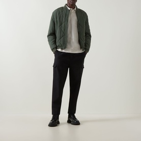 Model wearing Boss Green Label Light Beige polo, styled with dark green quilted bomber jacket, black cargo trousers and black chunky loafers.