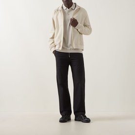Model wearing Boss Green Label Light Beige cotton polo, styled with cream zip jacket, black wide-leg trousers and dark leather shoes.