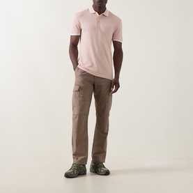 Model wearing Boss Green Label Paddy Logo Tipped Polo Shirt in light pastel orange, styled with taupe cargo trousers and green hiking shoes.