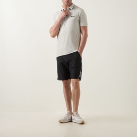 Model wearing Boss Green Label Paul Pro Logo Polo Shirt in light beige with black shorts and white trainers
