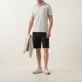 Model wearing Boss Green Label Paul Pro Logo Polo Shirt in Light Beige with black shorts, carrying a jacket, styled with grey trainers.