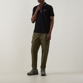 Model wearing Boss Green Label Philix GOC Logo Zip Polo Shirt in black with stripe zip collar, styled with olive cargo trousers and chunky trainers.