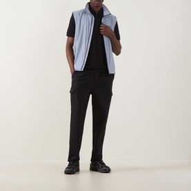 Model wearing Boss Green Label Urban Tech Logo Polo Shirt in black, styled with a light blue gilet and black cargo trousers.