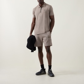 Model wearing Boss Green Label light green polo shirt with zip neck, styled with matching shorts, carrying dark jacket, navy trainers.