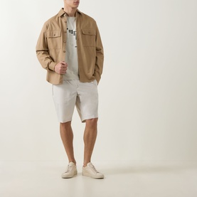 Model wearing Boss Green Label Light Beige shorts styled with a tan overshirt, graphic tee and cream trainers.