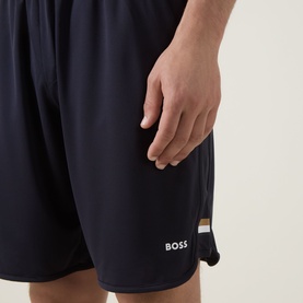 Model wearing Boss Green Label dark blue polyester shorts with gold and white stripe detail and embroidered logo at hem.