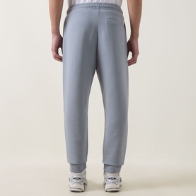 Model wearing Boss Green Label Hadiko Logo Track Pants in dark grey, rear view, with white cuffed ankles and trainers visible.