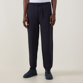Model wearing Boss Green Label JT Logo Sweatpants in dark blue, slim-leg with cuffed ankles and drawstring waist, styled with navy trainers.