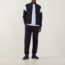 Model wearing Boss Green Label JT Logo Sweatpants in dark blue, slim-leg with cuffed ankles, styled with a navy varsity jacket and white tee.