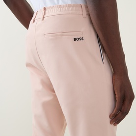 Model wearing Boss Green Label GOC Swing L Water-Repellent Trousers in light pastel orange, showing rear jetted pocket and logo detail.