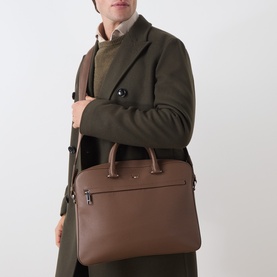 Model carrying Hugo Boss Ray S Doc Briefcase in medium brown grained finish with silver-tone hardware and top handles, styled with olive coat