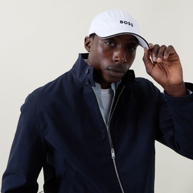 Model with Hugo Boss Lach-Toc-N Perforated Logo Cap in white, featuring curved visor and gloss logo lettering, styled with navy zip-up jacket