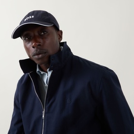 Model with Hugo Boss Lach-Toc-N Perforated Logo Cap in Dark Blue, curved visor, gloss BOSS lettering, styled with navy zip-up jacket