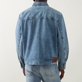 Model wearing Hugo Boss Orange Luney Denim Jacket in turquoise mid-wash denim, rear view showing logo patch, styled with light-wash jeans