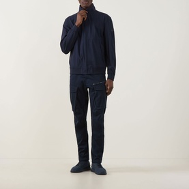 Model wearing Hugo Boss Orange Qlik Logo Windbreaker in dark blue with funnel neck and zip front, styled with navy cargo trousers and dark trainers.