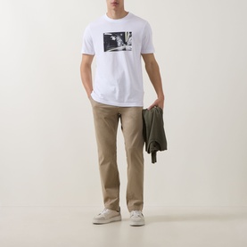 Model wearing Hugo Boss Orange light pastel brown cotton chino trousers, styled with white graphic tee, olive jacket and white trainers.