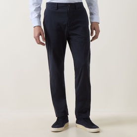 Model wearing Hugo Boss Orange dark blue cotton chino trousers with slim fit, styled with a light blue shirt and white trainers.