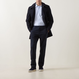 Model wearing Hugo Boss Orange dark blue cotton chino trousers, styled with a navy overcoat, light blue shirt and beige trainers.
