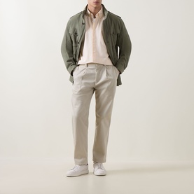 Model wearing Hugo Boss Orange light beige chino trousers with a pink hoodie, olive field jacket and white trainers.