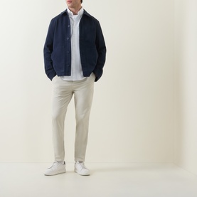 Model wearing Hugo Boss Orange Overdyed Tapered-Leg Chinos in light beige, styled with a navy jacket, light shirt and white trainers.