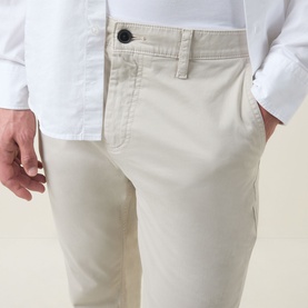 Model wearing Hugo Boss Orange Overdyed Tapered-Leg Chinos in Light Beige, styled with a white shirt. Mid-rise fit with side pocket detail visible.
