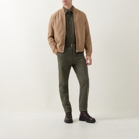 Model wearing Hugo Boss Orange Bright Green cotton chino trousers, styled with a camel bomber jacket, dark shirt, and brown lace-up boots.