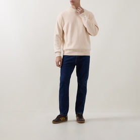 Model wearing Hugo Boss Orange Akapulko Logo Relaxed Fit Sweater in light pastel orange, styled with dark indigo jeans and brown trainers.