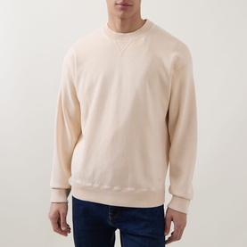 Model wearing Hugo Boss Orange Akapulko Logo Relaxed Fit Sweater in light pastel orange, crew neck, ribbed trims, styled with dark blue jeans.