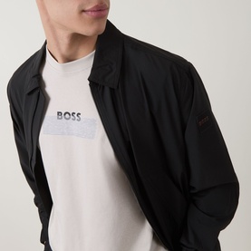 Model wearing Hugo Boss Orange Light Beige crew neck T-shirt with BOSS logo graphic, styled with a black bomber jacket.