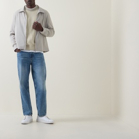 Model wearing Hugo Boss Orange Kosido Light Beige crew neck knit sweater, styled with a grey zip jacket, blue jeans, and white trainers.
