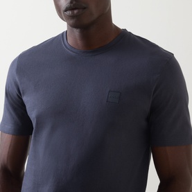 Model wearing Hugo Boss Orange Tales Logo T-Shirt in dark blue, crew neck with subtle logo patch on chest, short sleeves, 100% cotton.