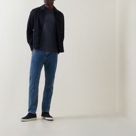 Model wearing Hugo Boss Orange Tales Logo T-Shirt in dark blue, styled with navy overshirt, blue jeans and navy slip-on shoes.
