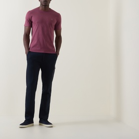 Model wearing Hugo Boss Orange Tales Logo T-Shirt in medium red with navy trousers and grey slip-on trainers.
