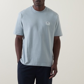 Model wearing Hugo Boss Orange Te Frame Logo Back Graphic T-Shirt in Open Grey, crew neck, short sleeves, with navy trousers.