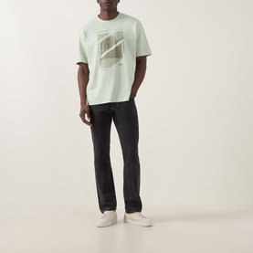 Model wearing Hugo Boss Orange Te Journey Relaxed Fit T-Shirt in Open Green with graphic print, styled with dark slim jeans and white trainers.