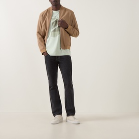 Model wearing Hugo Boss Orange Te Journey Relaxed Fit T-Shirt in Open Green with camel bomber jacket, dark jeans and white trainers.