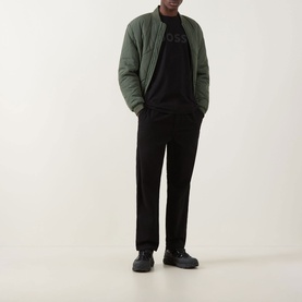 Model wearing Hugo Boss Orange Te Logo T-Shirt in black with tonal logo, styled with green quilted bomber jacket and black trousers.